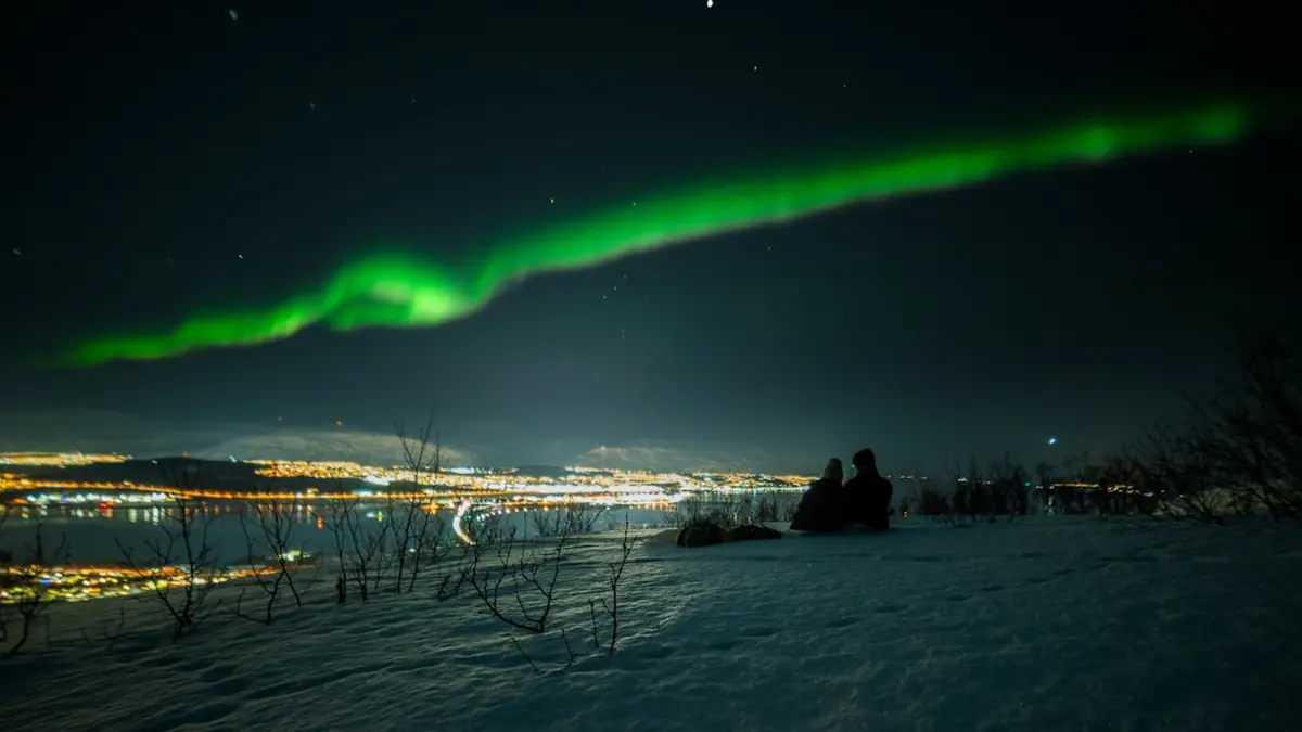 Nordlys over en opplyst by i Nord-Norge